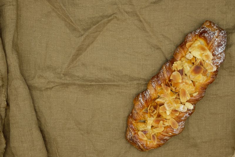 Fruit almond danish bun. Sweet pastry with caramelized apples or pears. Sprinkled with almonds. Dark goldenrod color linen fabric. Copy space. Top view.
