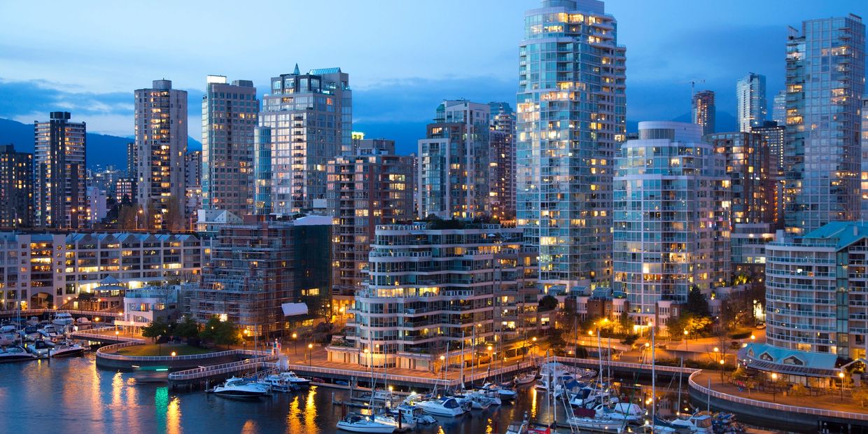 Evening view of a city skyline with illuminated buildings and boats at the waterfront.
