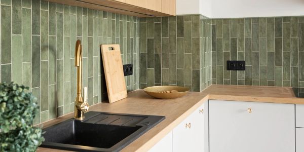 Modern kitchen corner with green tiled backsplash and wooden countertop.