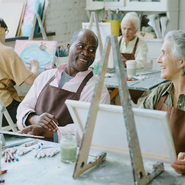 Adults enjoying a painting class together, smiling and interacting.