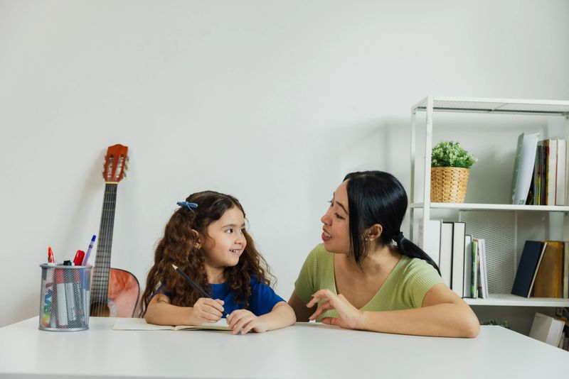 A mother engages with her daughter, assisting with homework at a tidy study table. The background features a guitar and neatly arranged books, creating a warm study atmosphere.