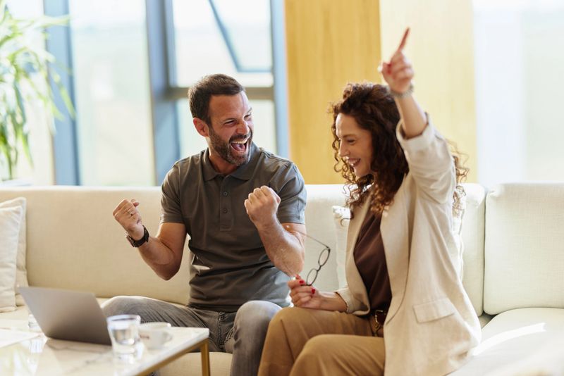 Cheerful entrepreneurs having fun while celebrating good news received over a computer at casual office. Focus is on man.