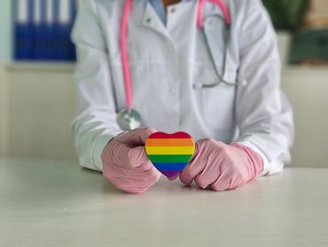 Doctor holding a heart with a rainbow pride flag design.