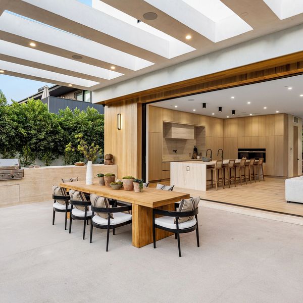 Modern outdoor dining area with wooden table, chairs, and built-in grill adjacent to an open-concept kitchen and living room.