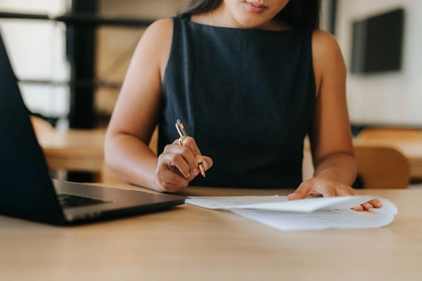 Mujer escribiendo en una mesa junto a una laptop.