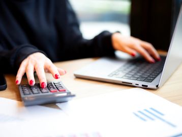 Person using calculator and laptop with painted nails.