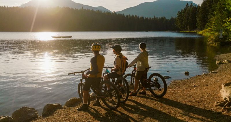 Family with mountain bikes pauses by lakeshore at sunset, Whistler, BC