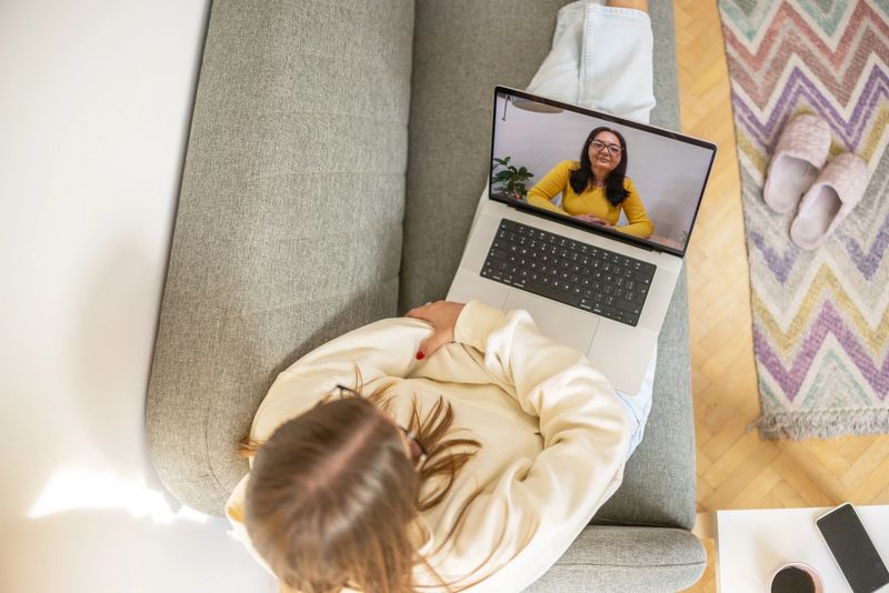 From the comfort of her home young woman sitting on sofa, her therapist offering  support through a digital connection