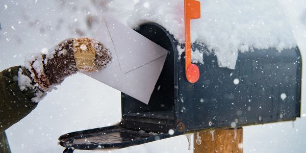 Person wearing mittens putting a letter in a snowy mailbox.