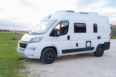 White camper van parked on a gravel road near grassy fields.