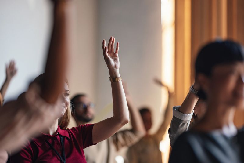 An attentive group of people actively participating in a business conference, raising their hands to engage with the speaker. The image captures a dynamic and interactive professional environment.
