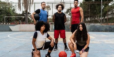 A diverse basketball team posing confidently on an outdoor court.