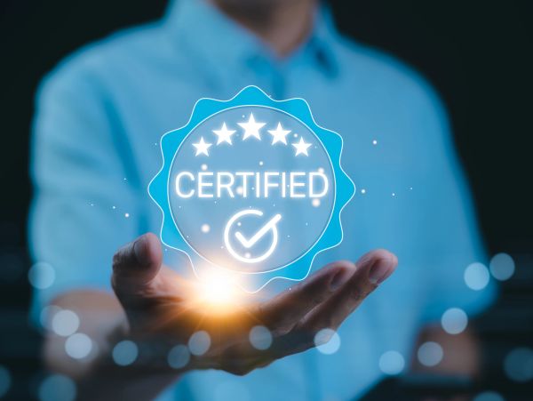Hand holding glowing certified badge with checkmark and stars.
