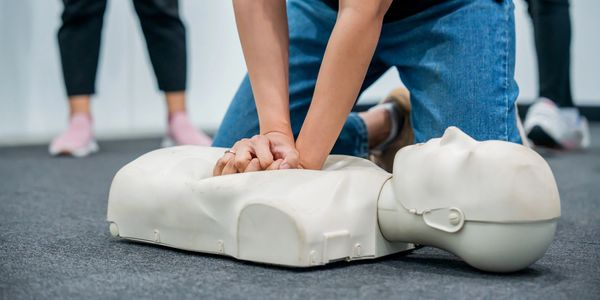 Person practicing chest compressions on a CPR training manikin during a first aid class.