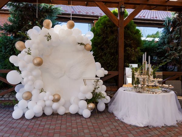 White and gold balloons decorate a party with angel wings and cake.