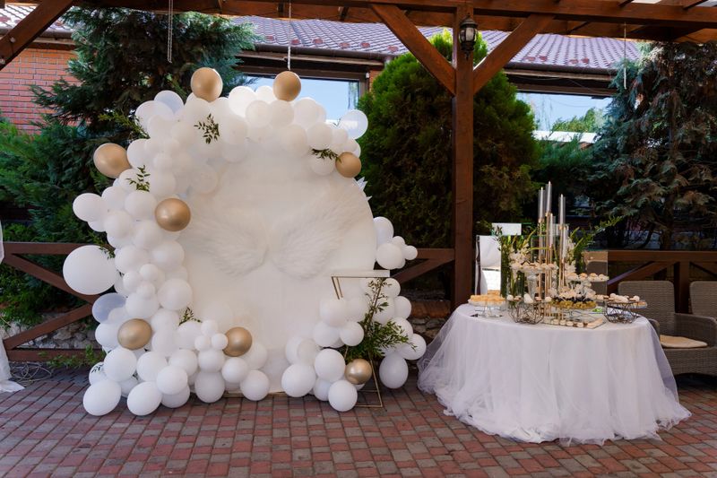 Elegant Outdoor Celebration Arrangement with White and Gold Balloon Decor and Dessert Table.