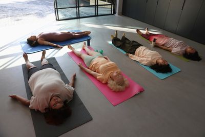 Five people lying on yoga mats indoors, practicing relaxation or meditation.
