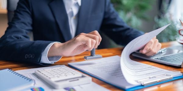 A person in a suit stamps a document at a desk filled with office supplies.