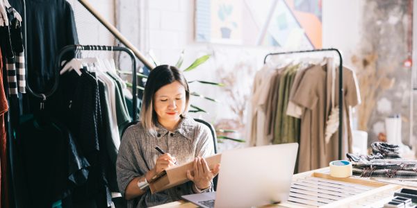Woman working in a clothing store with a tablet and laptop.