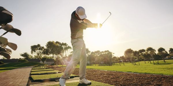 Golfer swinging club at sunset on golf course.