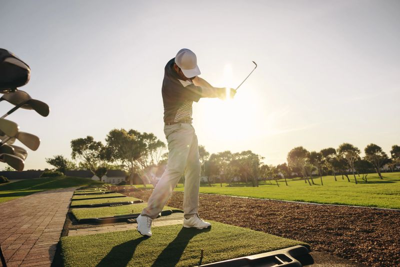 Captured in the midst of a powerful swing, a professional golfer practices under the brilliant sun on a serene golf course. Man hitting a shot at a golf driving range.