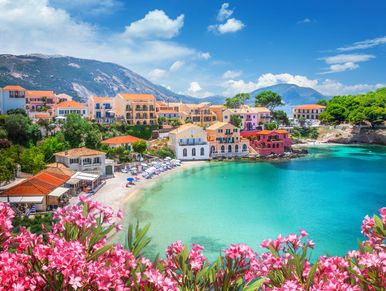 Colorful coastal village with turquoise water and pink flowers.