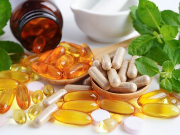 Various supplements including capsules, softgels, tablets, and fresh green leaves.