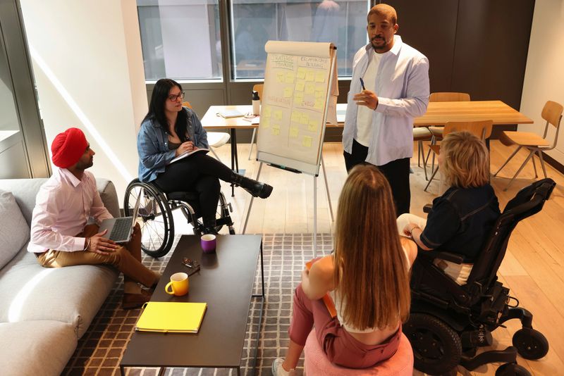 Diverse group of business people, two men and three women, two of women on wheelchairs, during presentation in office.