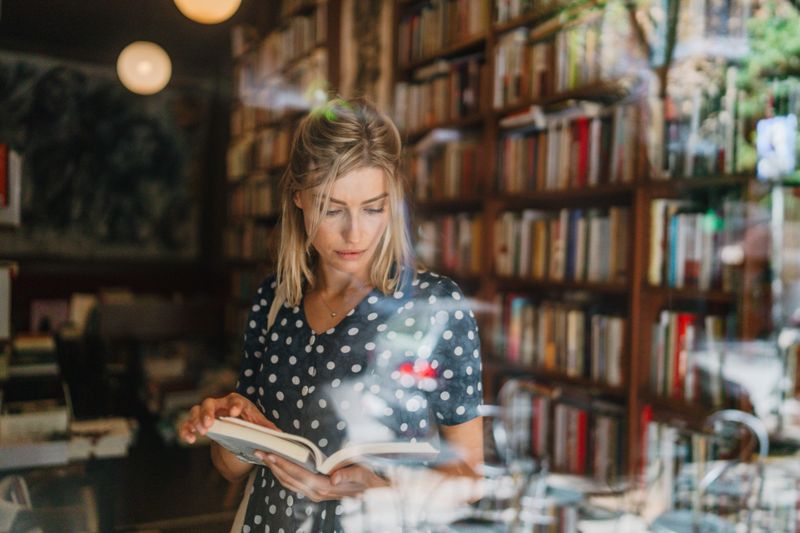 Photo of a mid adult woman, scrolling the books and looking for the favorite author and tittle in a local bookstore