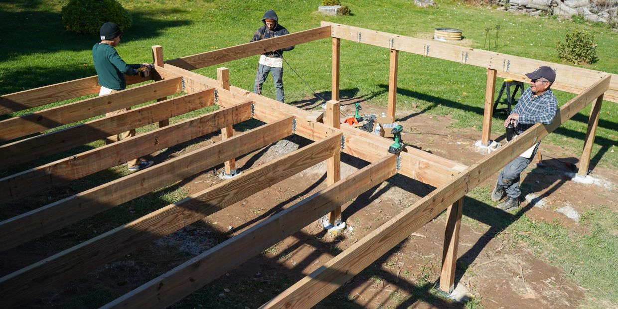 People building a wooden deck frame outdoors.