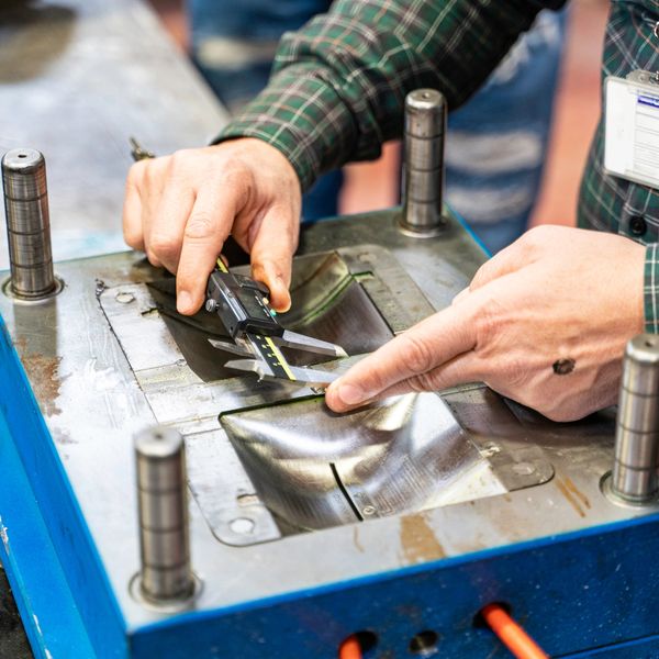 Person measuring metal mold with caliper.