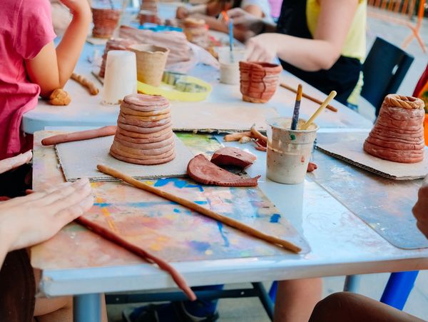 People working on pottery projects at a table with clay and tools.