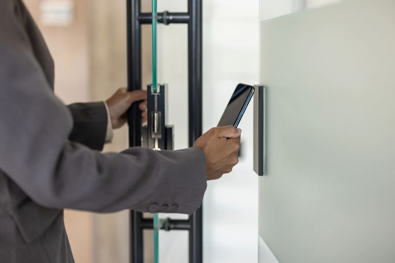 Confident professional using smartphone for secure entry into office environment. Person holding phone as key for access control, representing technology in workplace security. Concept mobile access.