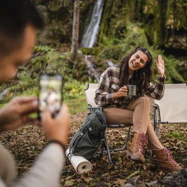 Woman smiling and waving while having a drink outdoors.