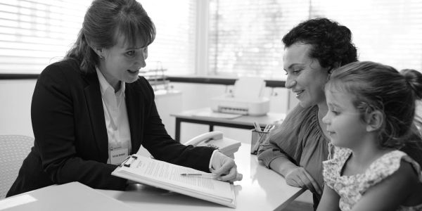 A professional woman explains documents to a mother and her daughter in an office.