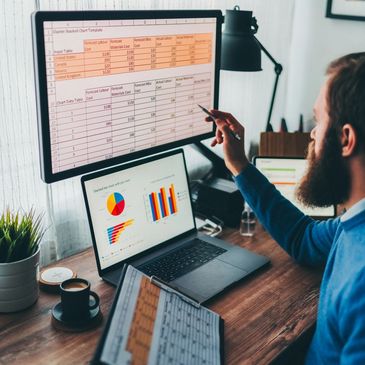 Ein Mann analysiert Finanzdaten auf einem Bildschirm und Laptop.