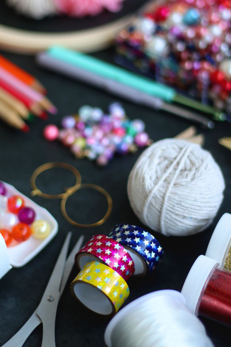 Colorful beads, coloring pencils, glitter, needles, string, hoop, tape and scissors on dark background. Various colorful craft supplies. Selective focus.