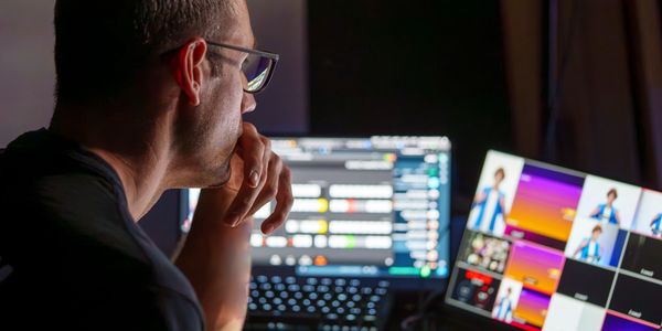 Man wearing glasses works intently at a dual-monitor setup with colorful displays.