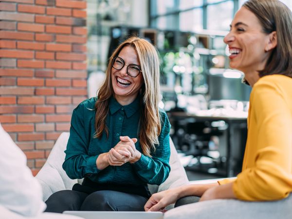 Three colleagues sharing a joyful moment in a modern office setting.