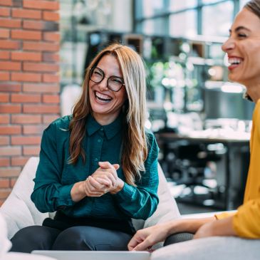 Two women smiling and laughing in a casual office setting.