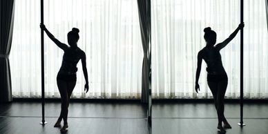 Silhouette of a woman dancing with a pole in a softly lit room.