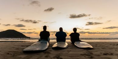 Three surfers sitting on surfboards at sunset.