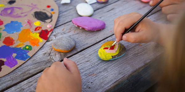 Child painting colorful designs on small rocks outdoors.