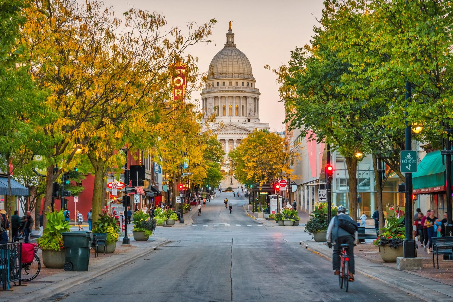 State Street in the City of Madison, lookin toward the Capitol building, with autumn trees and several bikers and walkers shown.