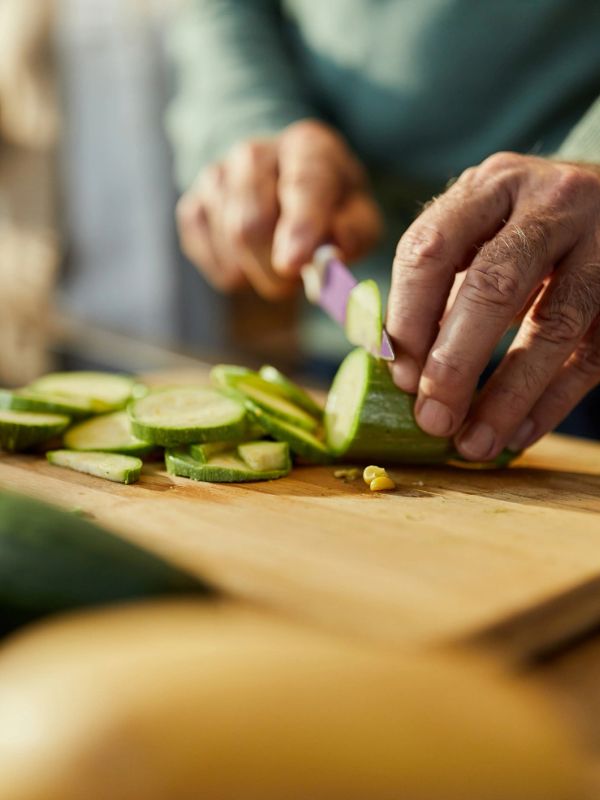 Hands slicing a cucumber on a wooden board.