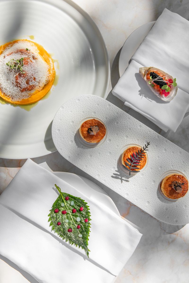 Michelin Fine dining restaurant Appetizers tasting menu at elegant gourmet table plates with puff pastries, caviar oyster, herb leaves and flavour gels