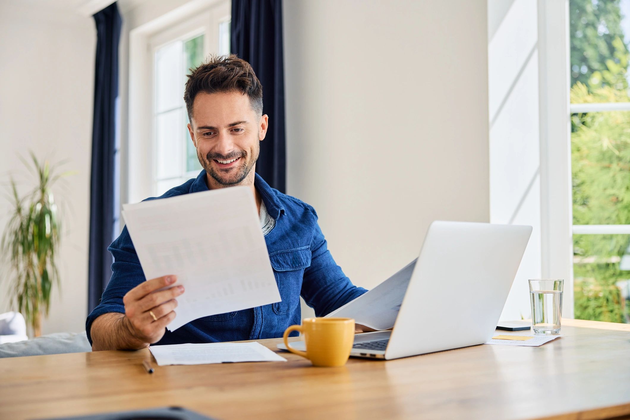 Business person with a laptop. Looking at a printed document and smiling