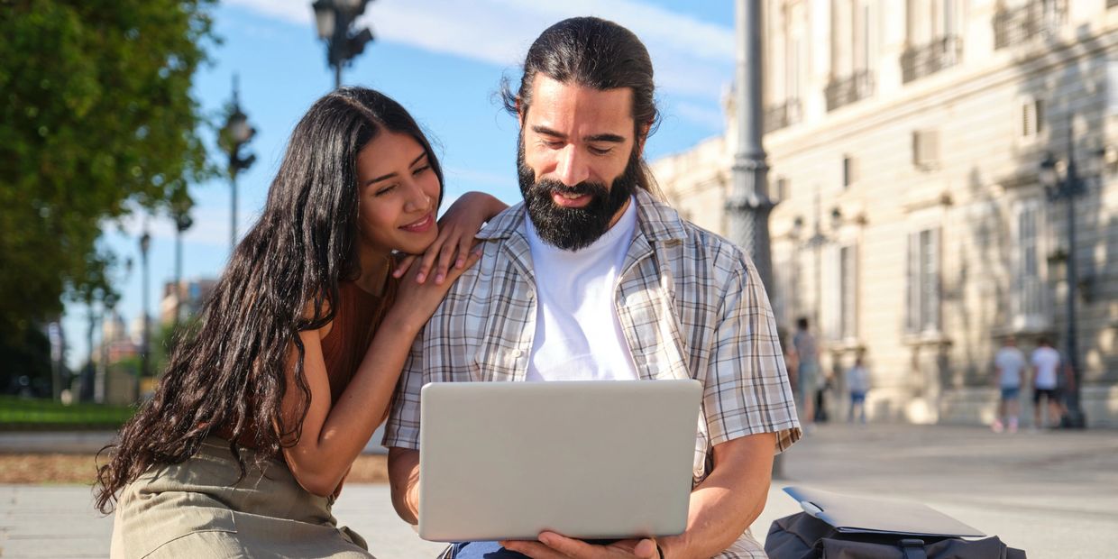 Couple looking at laptop outdoors, smiling.