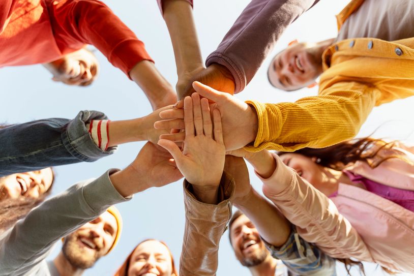 A group of diverse friends stacking their hands in unity outdoors.
