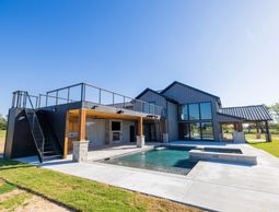 Modern house with a spacious outdoor pool and patio under a clear blue sky.